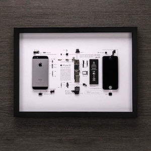 May include: A framed display of the disassembled parts of an iPhone 6, including the phone's screen, motherboard, battery, and other components. The parts are arranged in a grid pattern on a white background, with the phone's logo and model number visible at the top.