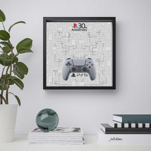 May include: A framed print featuring a white PlayStation 5 controller with the PlayStation logo and the text "PS5" on the controller. The background is a gray pattern with the text "30th Anniversary" and a PlayStation logo.