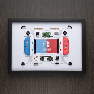 May include: A framed display of disassembled Nintendo Switch Joy-Con controllers. The display shows the individual components of the controllers, including the buttons, circuit boards, and plastic casings. The display also includes the Nintendo Switch logo and the text "JOY-CON".