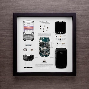 Op de afbeelding: Een ingelijst infographic dat de gedemonteerde onderdelen van een BlackBerry Curve 8310 smartphone laat zien. De infographic bevat het moederbord van de telefoon, het toetsenbord, het scherm en andere componenten. De tekst op de infographic luidt "BlackBerry Curve 8310, Geassembleerd in de VS."