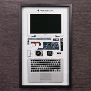 May include: A framed display of a disassembled MacBook Air laptop. The display shows the individual components of the laptop, including the screen, keyboard, motherboard, and hard drive. The quote "Sometimes life is going to hit you hard with a brick. Don't lose your mojo." is printed below the components.