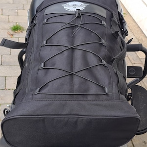 May include: Black motorcycle sissy bar bag with a skull and wings logo and a drawstring closure.
