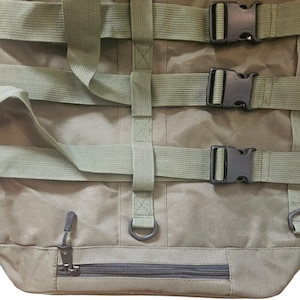 May include: A green canvas duffel bag with multiple adjustable straps and buckles. The bag has a zippered pocket on the front and a D-ring on each side.