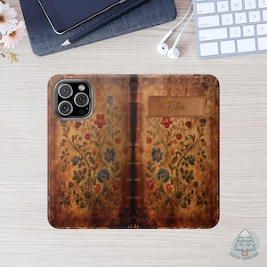 May include: A phone case with a vintage book cover design. The case features a brown background with floral patterns in red and blue. The name "Eileen" is printed on a rectangular label. The case is on a wooden surface.