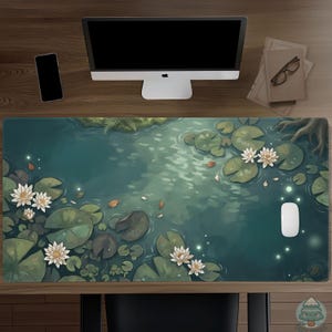 May include: A rectangular desk mat featuring a digital illustration of a pond surface with green lily pads, white water lilies, and small glowing light particles. The scene includes dark water, tree roots, and scattered leaves on the surface.