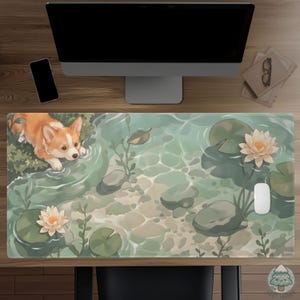 May include: A rectangular desk mat featuring a light green pond scene with a tan and white Corgi puppy looking into the water. The illustration includes light pink water lilies, green lily pads, smooth grey stones, and aquatic plants.