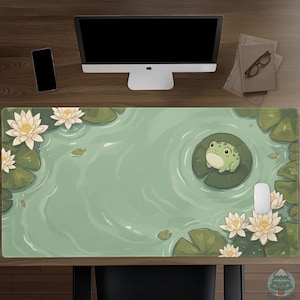 May include: A large desk mat featuring a serene pond scene with a cartoon frog on a lily pad. The mat has a light green background with white water lilies and green lily pads. A computer mouse and monitor are visible.