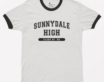 May include: A white ringer t-shirt with black trim on the collar and sleeves. The chest features black text that reads SUNNYDALE HIGH and CLASS OF '99 inside a black horizontal bar. A small North Star logo is printed on the inside neck label.