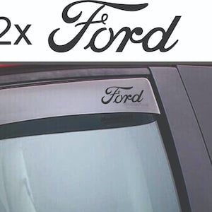 Puede incluir: Calcomanías negras con la fuente "Ford", con una segunda calcomanía que muestra "2x Ford". Las calcomanías se muestran en la ventana de un coche y sobre un fondo blanco.