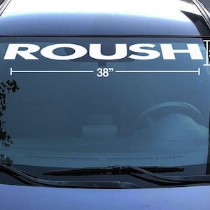 May include: White "ROUSH" windshield banner, 38 inches wide and 3.5 inches high, displayed on a car windshield. The banner is a bold, sans-serif font, designed for automotive enthusiasts.