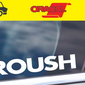 May include: White "ROUSH" decal on a car window. The text is in a bold, sans-serif font. The background is a blurred view of the outside world.