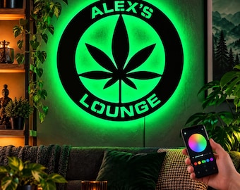 Pode incluir: Uma placa de parede circular de metal preto com um design de folha de cannabis recortado no centro e o texto ALEX'S LOUNGE arqueado ao redor, iluminada por uma luz LED verde brilhante que projeta um brilho na parede.