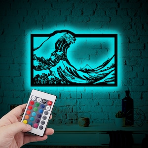 Puede incluir: Una silueta en blanco y negro de la Gran Ola de Kanagawa, una famosa estampa japonesa en madera, se ilumina con una luz azul brillante. La imagen está montada en una pared de ladrillo y se controla con un mando a distancia con múltiples opciones de color.