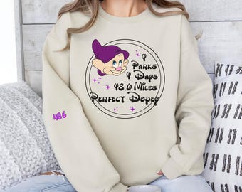 May include: A beige sweatshirt with a purple and black graphic of a cartoon character. The graphic includes the text "4 Parks 4 Days 48.6 Miles Perfect Dopey".