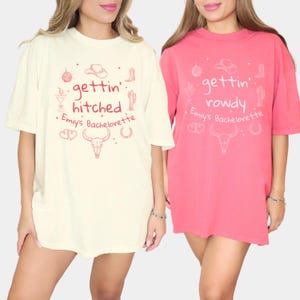 May include: Two oversized t-shirts with a western theme. One is cream with the text "gettin' hitched + Emiy's Bachelorette" and the other is pink with the text "gettin' rowdy + Emiy's Bachelorette".