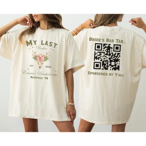 May include: Cream-colored t-shirt with text and graphics. The front features "MY LAST Rodeo" above a floral skull design, "Emma's Bachelorette," and "Nashville, TN." The back displays "BRIDE'S BAR TAB..." with a QR code and "SPONSORED BY Y'ALL."