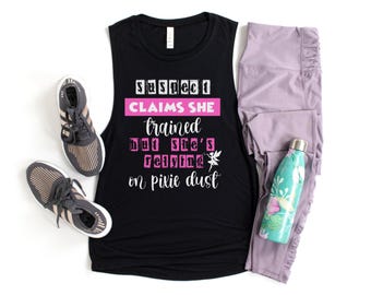 May include: Black muscle tank top with the text "Suspect Claims She Trained But She's Relying on Pixie Dust." Also pictured are gray sneakers, lavender leggings, and a teal water bottle.