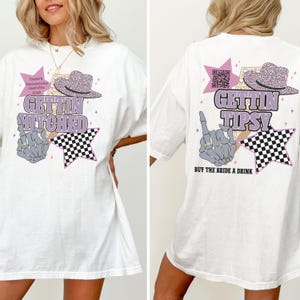May include: White t-shirt with a graphic design for a bachelorette party. The front says "Gettin' Hitched" with a hat, star, and skeleton hand. The back says "Gettin' Tipsy" with a hat, star, skeleton hand, and "Buy the Bride a Drink."