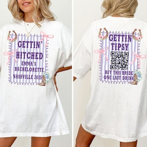 May include: White t-shirt with text and graphics for a bachelorette party. The front says "Gettin' Hitched" with "Emma's Bachelorette Nashville 2025". The back says "Gettin' Tipsy" with a QR code and "Buy This Bride One Last Drink".