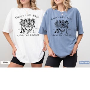 May include: Two women wearing white and blue jean t-shirts with a black and white graphic print of four women walking. The text on the shirts reads "Emily's Last Bash est 2025 Watch Out Nashville".