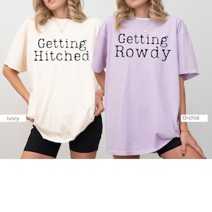May include: Two oversized t-shirts with the text "Getting Hitched" and "Getting Rowdy" printed on them. The shirt on the left is ivory and the shirt on the right is orchid.