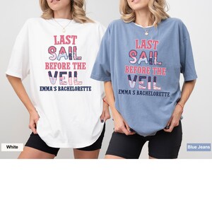 May include: Two white and blue t-shirts with the text "Last Sail Before the Veil" and "Emma's Bachelorette" printed on them. The shirts are worn by two women, one wearing a white shirt and the other wearing a blue shirt.