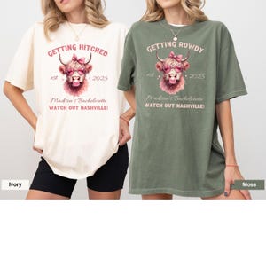 May include: Two oversized t-shirts with a cow graphic and text that reads "Getting Hitched" and "Getting Rowdy". The shirts are in ivory and moss green.