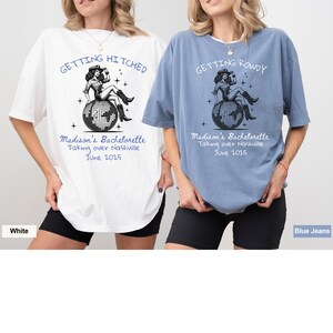 May include: White and blue t-shirts with text and graphics. The white shirt says "Getting Hitched" and the blue shirt says "Getting Rowdy". Both shirts have a graphic of a woman on a disco ball and text that says "Madison's Bachelorette Taking over Nashville June 2025".