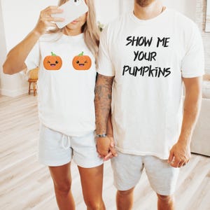 May include: White t-shirts with pumpkin graphics and the text "Show Me Your Pumpkins." The shirts are paired with gray shorts. The pumpkin graphics are orange with green stems and smiling faces.