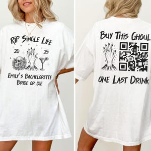 May include: White t-shirt with black text and graphics. The front reads "RIP SINGLE LIFE" with a skull, roses, and a cocktail glass. The back says "Buy This Ghoul" with a QR code and "ONE LAST DRINK".