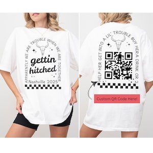 May include: White t-shirt with a black graphic that says "Apparently we are trouble when we are together, gettin hitched, Nashville 2025". The back of the shirt has a black and white QR code with the text "Help her get into a lil' trouble buy her a drink or 2".