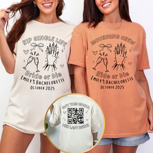 May include: Two t-shirts, one cream and one orange, with black graphic designs. The cream shirt says "RIP SINGLE LIFE" and "Bride or Die" with a hand, champagne glasses, and hearts. The orange shirt says "MOURNING CREW" and "Ride or Die". The back of the cream shirt says "BUY THIS GHOUL".