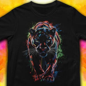 May include: Black t-shirt featuring a colorful illustration of a panther. The panther is depicted with vibrant hues of red, blue, green, and yellow, with paint splatter effects. The design is centered on the shirt.