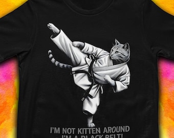 May include: Black t-shirt featuring a gray cat in a karate uniform performing a high kick. The cat is wearing a white gi and a black belt. Text on the shirt reads, "I'M NOT KITTEN AROUND - I'M A BLACK BELT!"