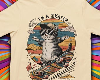 May include: Cream-colored t-shirt featuring a cartoon cat wearing sunglasses and a cap, riding a skateboard. The design includes the text "I'M A SKATER" above the cat, set against a colorful sunset background with clouds.