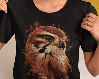 May include: Black t-shirt featuring a detailed illustration of a hawk's head, rendered in shades of brown and tan, surrounded by brown floral accents. The hawk's eye is visible, and the beak is black. A nature-themed graphic tee.