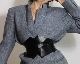 May include: A blue and white herringbone blazer with a black leather corset belt. The blazer has a high collar and long sleeves.