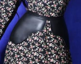 Puede incluir: Un vestido negro de manga larga con un pequeño estampado floral en rosa, blanco y verde, combinado con un corsé de cintura negro liso. El vestido presenta un cuello redondo y puños fruncidos, creando una silueta estructurada.