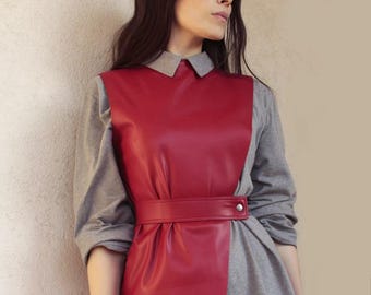 May include: A red leather vest with a gray shirt underneath. The vest has a belt with a silver buckle. The model is wearing a white collared shirt underneath the vest.