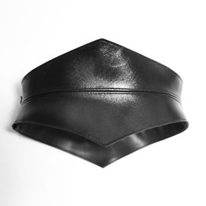 May include: A black leather belt with a pointed, V-shaped front. The belt is made of a smooth, shiny leather and has a simple, minimalist design.