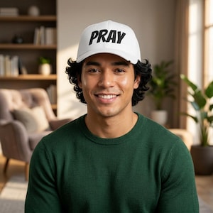 Puede incluir: Una gorra de béisbol blanca con la palabra PRAY impresa en letras mayúsculas negras y negritas en el panel frontal. La gorra tiene una corona estructurada, una visera curva y un pequeño detalle de etiqueta negra en el lateral de la visera.