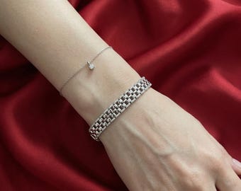 May include: A silver bracelet with a rectangular link design and a delicate chain bracelet with a small diamond pendant. The jewelry is displayed on a red satin background. A silver ring with small diamonds is also visible.