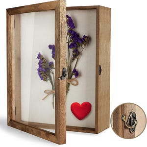 May include: A wooden shadow box with a glass front, displaying dried purple flowers tied with twine and a red heart. The box has a hinged door with a metal latch, perfect for displaying keepsakes or floral arrangements.