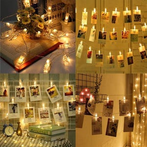 May include: String lights with small clear clips holding photos. The lights are warm white and are draped over a wall, books, and a table. Some photos are visible, and the overall effect is cozy and decorative.