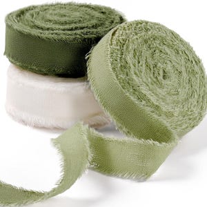 May include: Three spools of frayed-edge ribbon arranged in a stack and a single roll. The ribbons are in shades of dark olive green, cream white, and a lighter sage green. Each spool features a textured, woven fabric with loose, raw edges.
