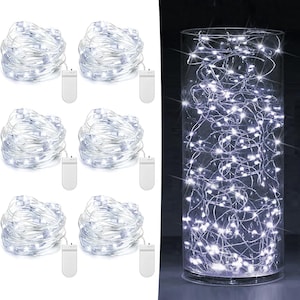May include: Six coils of silver wire fairy lights, each featuring a small white battery pack with an on-off switch. A tall, clear cylindrical glass vase is filled with a single strand of these bright white LED lights, creating a glowing effect.
