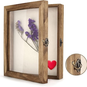 May include: A wooden shadow box with a hinged glass door, displaying dried purple flowers and a red heart. The box has a rustic, natural wood finish and a metal clasp closure. The box is designed to display small objects.