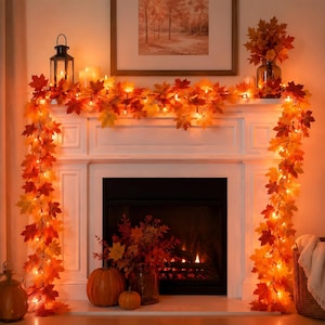 May include: An artificial maple leaf garland featuring warm orange, red, and yellow foliage intertwined with small glowing string lights. The garland drapes across a white fireplace mantel, accented by a black lantern and a glass vase of leaves.