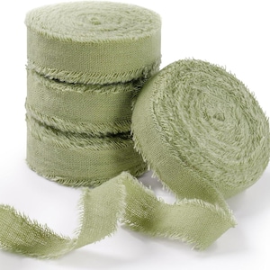 May include: A stack of three sage green fabric ribbon rolls and one additional roll placed to the right, all featuring a textured weave and frayed, raw edges. The ribbon is unwound at the bottom, displaying the consistent light green color.