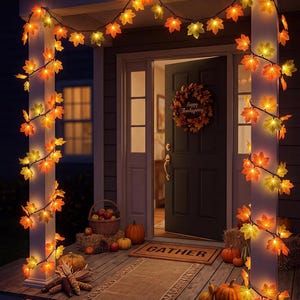 May include: A string of LED lights featuring artificial maple leaves in shades of orange, yellow, and red wrapped around two white porch columns. A dark door features a wreath with the text Happy Thanksgiving and a mat with the word GATHER.